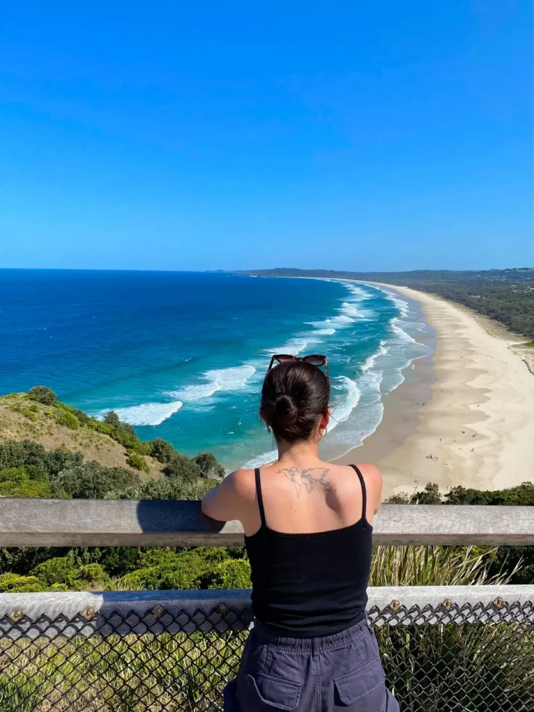 photo prise à Byron Bay durant mon PVT en Australie. Image qui illustre le blog PVT en Australie et au Japon de Goldenturtles. moi regardant l'océan, avec ma map monde dans le dos.